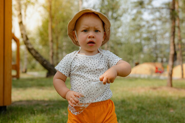 Thirst, dehydration. Cute little boy drinks water from a plastic bottle against on the playground....