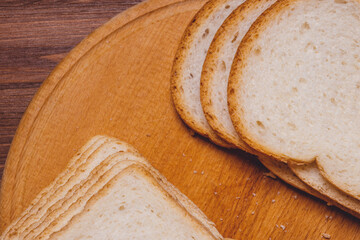 Sliced white bread with brown crust closeup on a wooden board on the dark wooden table. Top view