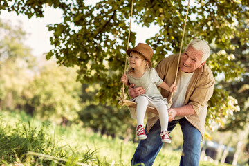 Young girl and her grandfather playing on a swing in the park