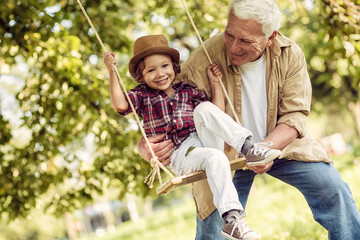 Young boy and his grandfather spending time in the park on a swing