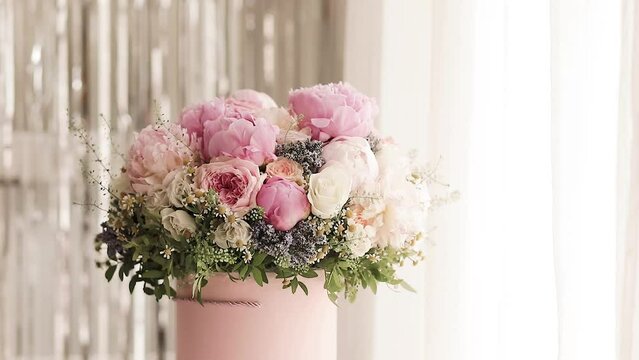An elegant bouquet of fresh roses, peonies, and daisies in a pink box, beautifully arranged and placed by a light-filled window.