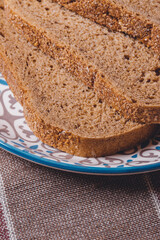 Sliced brown bread covered with bran in a plate on a tablecloth.