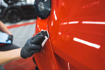 closeup shot of a car specialist cleaning a red car at the repair shop. High quality photo