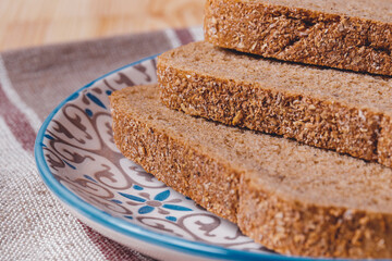 Sliced brown bread covered with bran in a plate on a tablecloth.