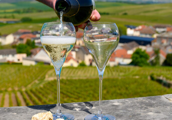 Pouring of grand cru sparkling white wine with bubbles champagne with view on houses and vineyards grand cru wine producer small village Cramant, Champagne, France