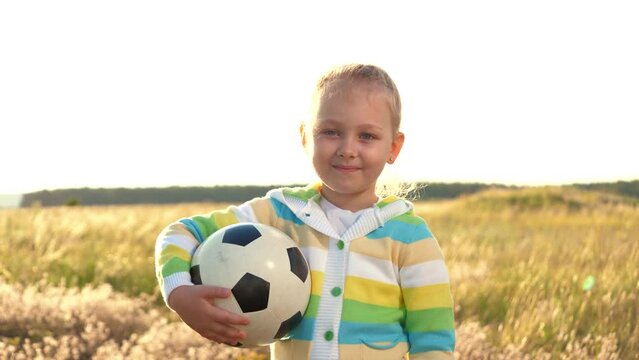 close-up portrait smiling girl. face child smile. soccer ball child daughter holds hands sunset field. football game. sports children dream lifestyle. little kid daughter with ball hands smiles green