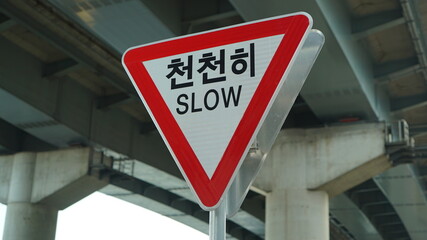 Road sign under a bridge over the Han River in Seoul, South Korea, text means slow down