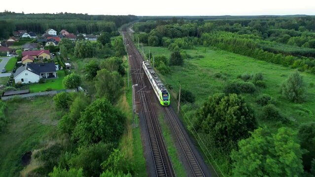 Train crossing the bridge and arriving on a train station platform in tranquil town full of trees, aerial dron view