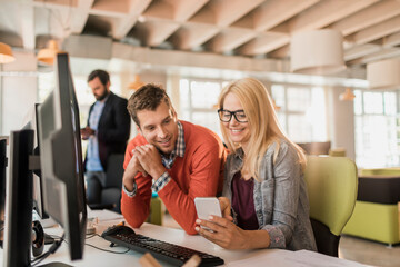 Young man and woman using a smart phone while working in a startup company office