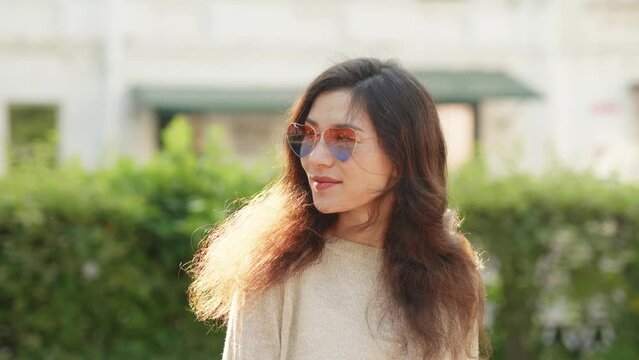 Concept of fashion style and street lifestyle. Pretty smiling asian woman in stylish look put on her trendy rose heart shape sunglasses. Beautiful portrait girl in bright sunlight during summertime.