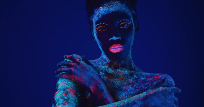 sexy woman in fluorescent paint makeup hugging herself close up portrait Slow motion isolated dark background