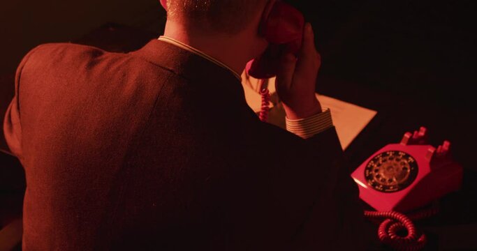 Unidentified man behind desk on corded rotary phone. Man hangs up rotary phone. Stylistic spy movie or film noir. (Shot on RED) 4K