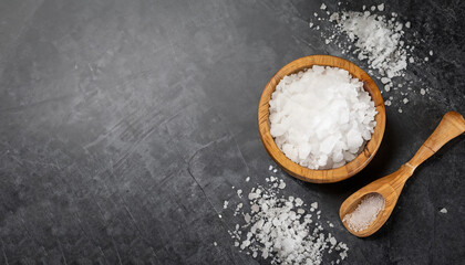 Salt in wooden olive bowl with scoop on stone table. Salt top view. Sea salt on black background.