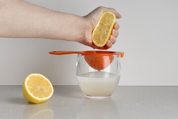 making lemon water, hand squeezes a half lemon over a strainer on a glass of water, a daily healthy habit for vitamin c, whie background with copy space