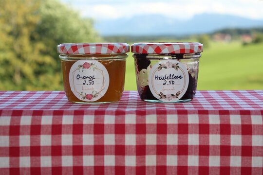 Selbstgemachte Marmelade, gekauft auf dem Wochenmarkt von einer Bäuerin. Heidelbeere und Orange. Allgäu und Bayern Landschaft im Hintergrund.