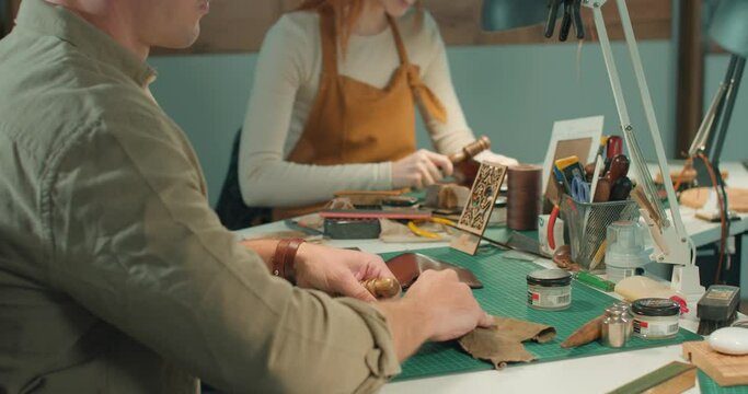 talented ginger girl burnishing edges of leather, man cleans material, craftswoman working, using edge slicker, necessary tools for tailor, accurate process of sewing, making wallet