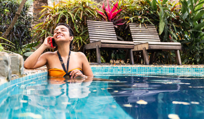 Joyful Latina Woman Talking on Phone in Tranquil Natural Resort Pool © Germán Camelo