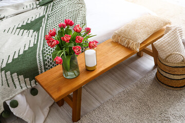 Vase with blooming tulips on wooden bedside bench in bedroom