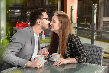 Beautiful happy loving couple sitting in restaurant, drinking coffee and kissing on sunny spring day