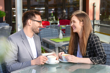 Beautiful happy loving couple sitting in restaurant and drinking coffee on sunny spring day