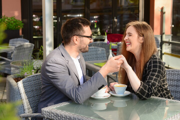 Beautiful happy loving couple sitting in restaurant, drinking coffee and holding hands on sunny spring day