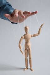 Woman pulling strings of puppet on light grey background, closeup