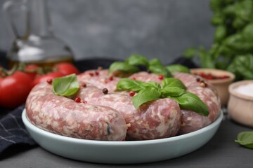 Raw homemade sausages, basil leaves and peppercorns on grey table, closeup