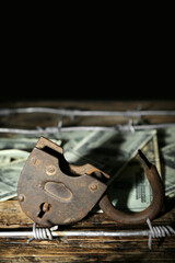 Lock with barbed wire and dollar banknotes on dark wooden table, closeup. Sanctions concept