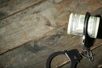 Handcuffs with dollar banknotes on dark wooden background. Sanctions concept