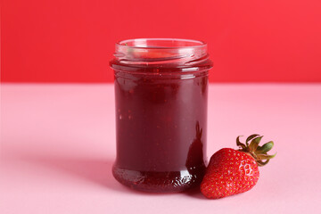 Jar of sweet strawberry jam on color background