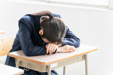 学校の教室で女子高校生・中学生が俯いて悩んでいる（悩む・困る・ストレス）
