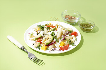 Plate of tasty pasta salad with tomatoes and avocado on green background