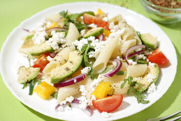 Plate of tasty pasta salad with tomatoes and avocado on green background