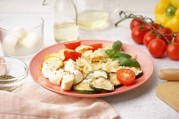 Plate of tasty pasta salad with tomatoes and basil on white background