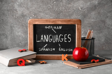 Blackboard with different languages and stationery on grunge grey table