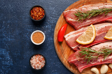 Wooden board with raw pork ribs, rosemary and spices on dark color background, closeup
