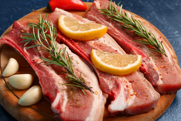 Wooden board with raw pork ribs, rosemary and spices on dark color background, closeup