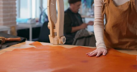 tailor in apron unrolls natural leather sheet at table in manufacturing workshop closeup. woman checking the quality of material Making craft accessories in studio. Girl with creative hobby Slow