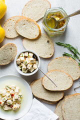 Top view of marinated feta cheese cubes and slices of toasted bread on a white plate. Cheese cubes in a ramekin with bread, flat lay of feta cheese cubes and slices of toast
