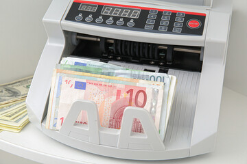 Cash counting machine with euro banknotes on shelf in office, closeup