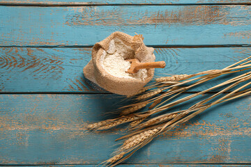 Sack bag with flour and wheat ears on blue wooden background