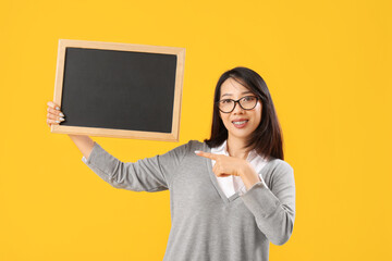 Female Asian teacher pointing at chalkboard on yellow background