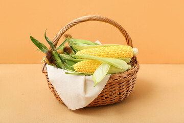 Wicker basket with fresh corn cobs on brown background
