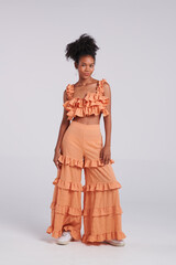 In a captivating fashion fusion, a Thai American black woman stuns in a fashionable orange dress during a studio shoot.