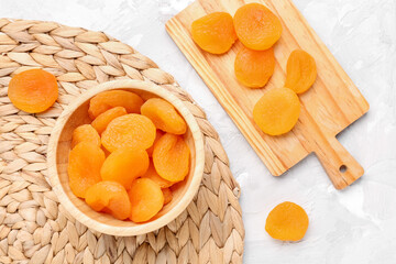 Wooden board and bowl with tasty dried apricots on white background