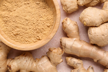 Fresh ginger roots and wooden bowl with dried powder on pink background