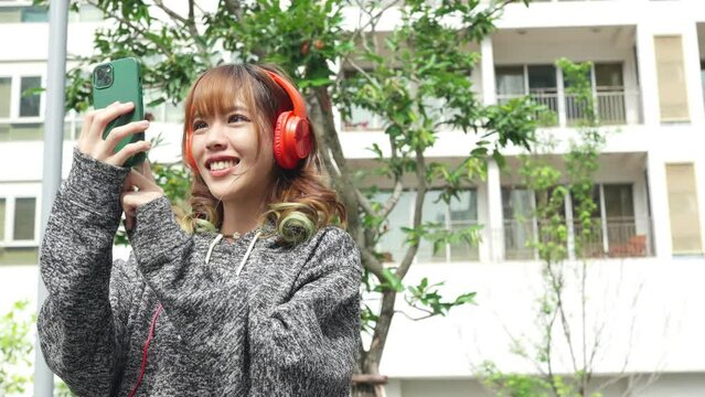 Asian woman listening to the music on headphones and using mobile phone during travel in the city. Attractive girl enjoy urban outdoor lifestyle with using digital gadget device and online network.