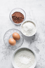mise en place of ingredients for making chocolate cake, top view of sugar, eggs, cocoa powder, flour on a marble table, process of making chocolate cake