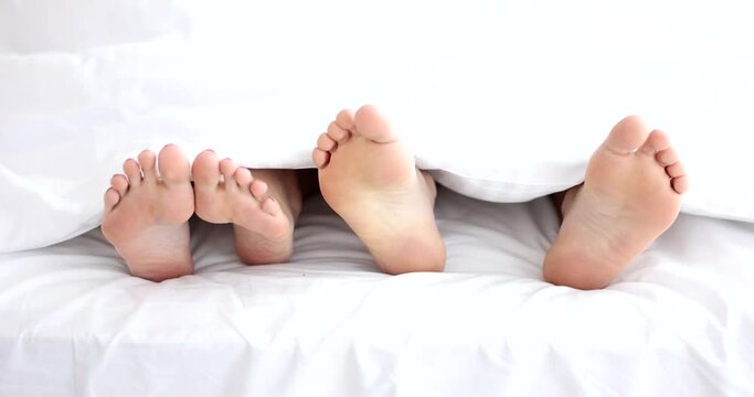 Male and female feet under a white blanket, close-up. Sexual relations, comfortable bed in the hotel