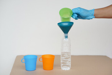 Closeup hand wear blue glove holds green mug to pour water into bottle to do science experiment....